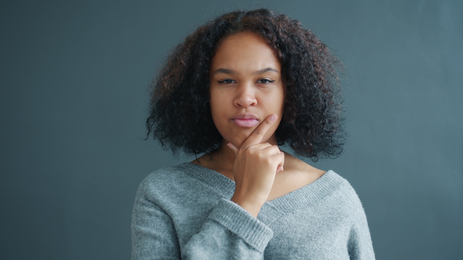 Young woman with hand on chin, looking thoughtful.